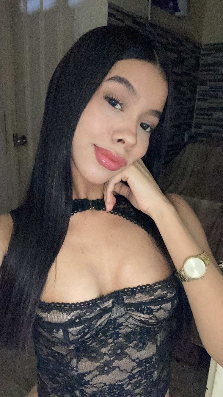 Woman with long dark hair in a black lace top, resting her chin on her hand