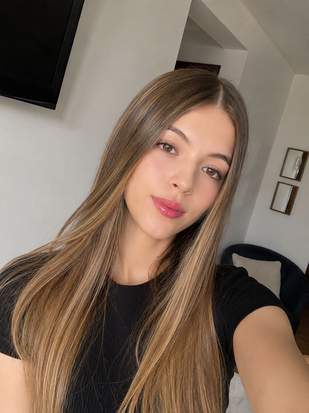 Woman with long hair in a black top taking a selfie at home