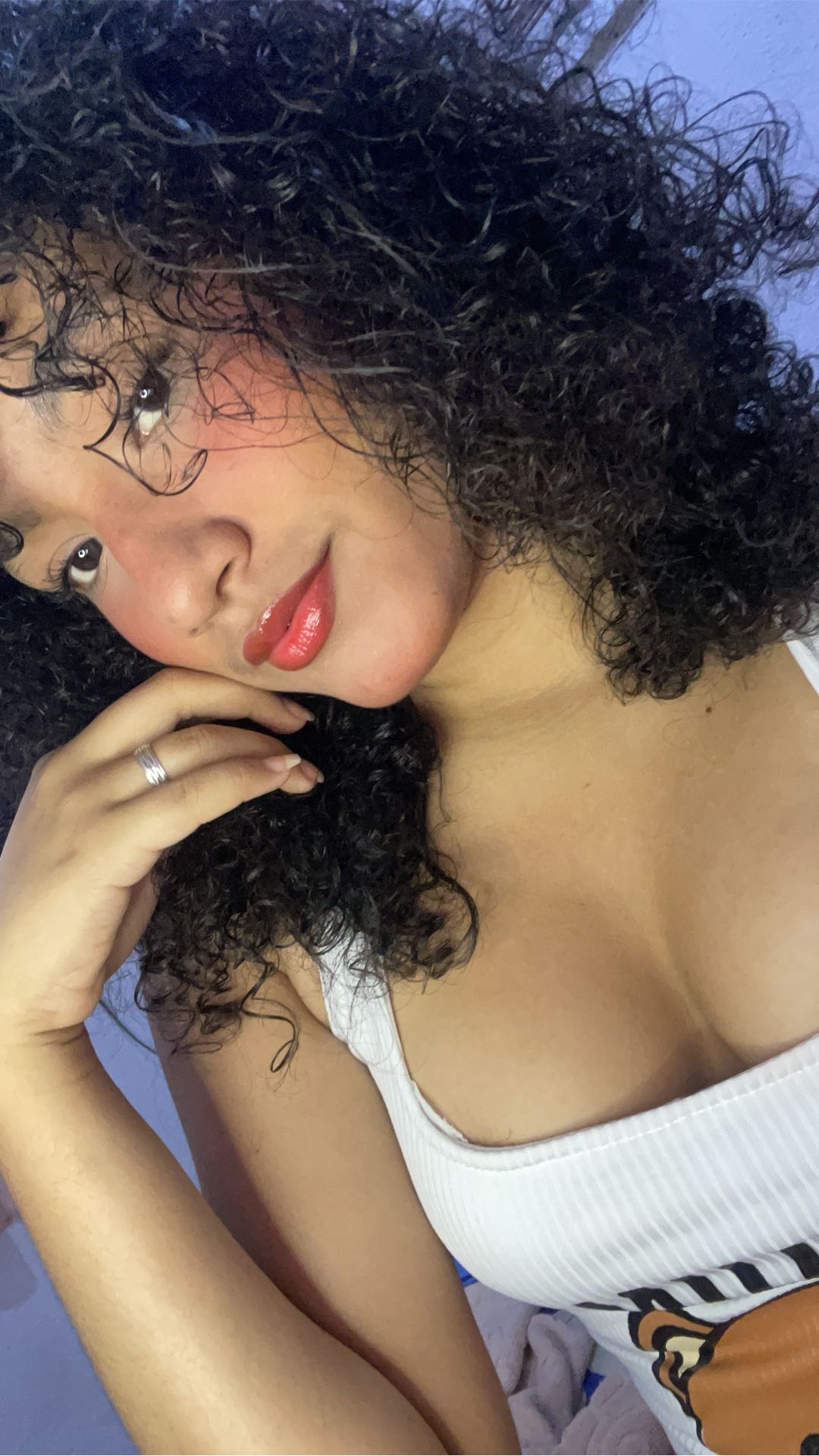 Woman with dark curly hair and glasses in a white top, hand at her face