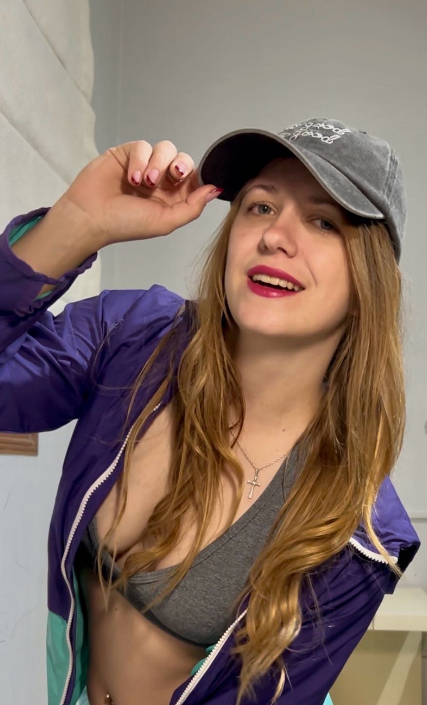 Woman in a grey cap and purple jacket, smiling at the camera